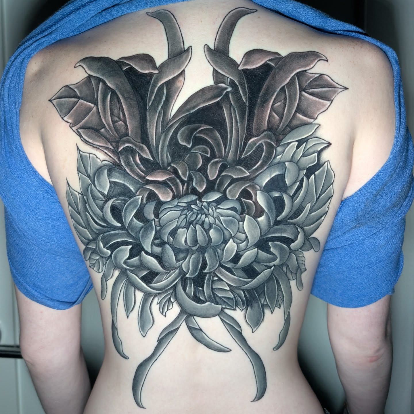 Finished floral tattoo across the upper back, black and grey.